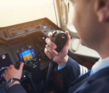 Close up pilot hand taking by portable radio set in cabin while navigating plane. Occupation and communication concept